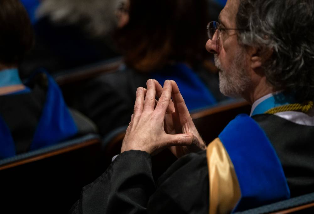 Faculty member sitting with fingertips together watching the program